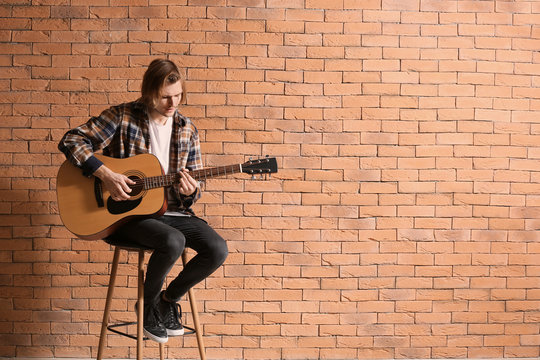 Handsome young man playing guitar against brick wall