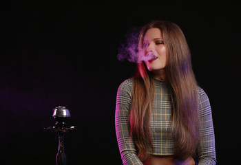 Young woman smoking hookah on dark background