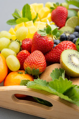 Close up mix fruits - mango, grapes, tangerine, lime, strawberry, kiwi, mint, on wooden tray and a gray background.
