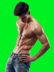 Fototapeta premium Attractive strong athletic brunette young man model in jeans showing press, torso, six pack abs and holding his hand on hips, looking down, isolated on chroma key background. Horizontal studio shot.
