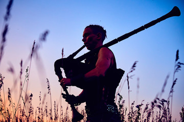 A young modern man plays musical bagpipes outside. Siluet