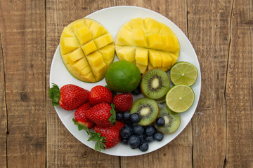 A plate with mixed fruit isolated on white background. Grapes, strawberry, mango, lime, kiwi, lime, citrus, blueberry, berry.