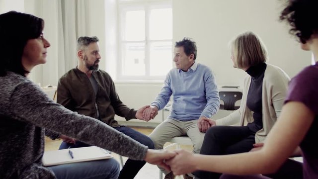 Men and women sitting in a circle during group therapy, supporting each other.