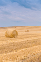 Fototapeta premium Hay bales under a cloudy sunset sky on a harvested wheat field.