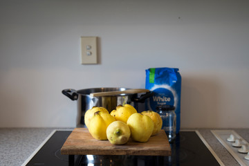 Obraz na płótnie Canvas Freshly picked homegrown organic yellow quinces with big stainless steel stock pot, sugar and empty jar, with wooden chopping board on stove top.
