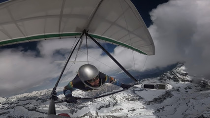 Hang glider pilot fly with his wing on high altitude between clouds above snow mountain peaks.