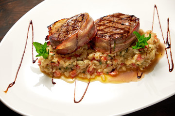 Meat medallions in bacon with rice. Dark wooden background. Restaurant menu