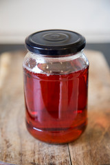 Homemade quince jelly in a glass jar with a black lid sitting on a wooden chopping board. It is made with imperfect, organic homegrown fruit. The clear ruby red color comes from the tannins.