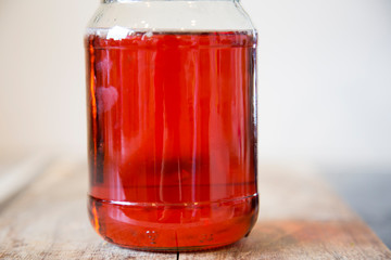 Fototapeta na wymiar Homemade quince jelly in a glass jar with a black lid sitting on a wooden chopping board. It is made with imperfect, organic homegrown fruit. The clear ruby red color comes from the tannins.