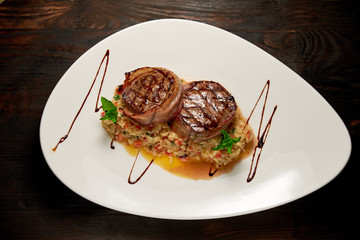 Meat medallions in bacon with rice. Dark wooden background. Restaurant menu