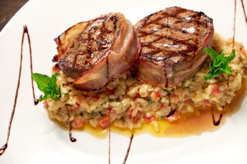 Meat medallions in bacon with rice. Dark wooden background. Restaurant menu