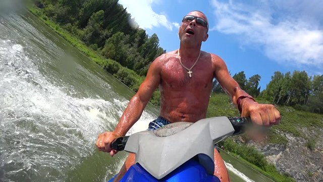 muscular guy on a jet ski. riding a jet ski on a mountain river. beautiful squall of water close-up, splashes of water and turns on jet ski. front view. bright sky. stock videos. super slow motion