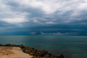 Pre-stormy sky sea smoothness. Seascape with horizon line and dark thunderclouds. View from stone beach with a dark sky