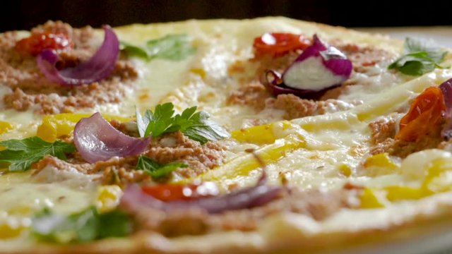Italian food. Delicious traditional pizza topped with cream sauce, fresh parsley, dried tomatoes, red onion, parmesan cheese, bell pepper, minced beef meat, cumin seeds. Slow motion. HD
