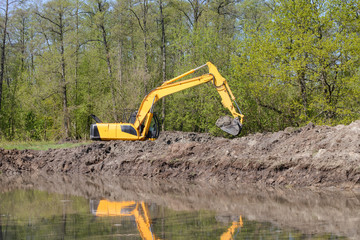 Excavator working near big hole fillled with water in the countryside