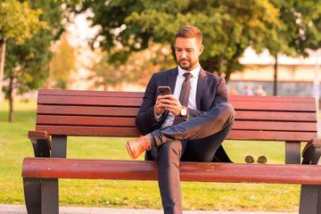 Fototapeta premium A businessmen sitting on a bench and using his smartphone
