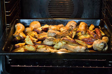 Roasting dish in oven with roasted cooked chicken drumsticks and red kumara seasoned with rosemary, smoked sea salt and white pepper.