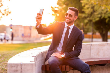 A businessman sitting on a bench and taking a selfie