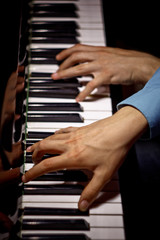 Fototapeta na wymiar two male hands on the piano. palms lie on the keys crosswise and play the keyboard instrument in the music school. student learns to play. hands pianist. black dark background. top view. vertical