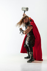 Long hair and muscular male model in leather viking's costume with the big hammer cosplaying Thor isolated on white studio background. Full-lenght portrait. Fantasy warrior, antique battle concept. - obrazy, fototapety, plakaty