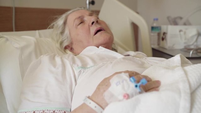 An old lady is sleeping and resting in hospital with scalp vein needle on her hand.