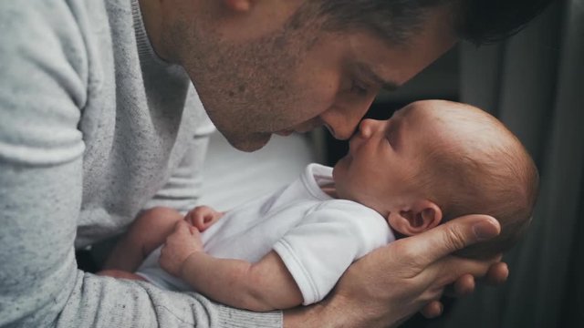New daddy snuggles and loves on his brand new baby boy while holding the tiny infant on his arms. Instant love between a father and child. Father in awe of his little child.