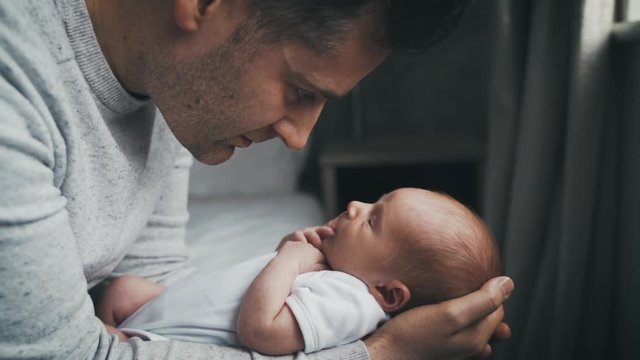 Newborn baby boy in the arms of his father. Daddy and son stare at each other as they bond. Love between parent and child from the first moment.