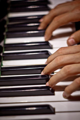 Obraz premium two male hands on the piano. palms lie on the keys and play the keyboard instrument in the music school. student learns to play. hands pianist. black dark background. top view. vertical