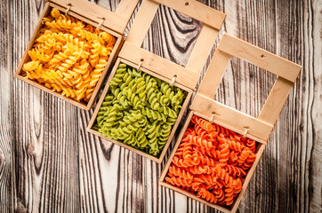 Multi-coloured pasta in the form of spirals lies in square wooden boxes that stand on a table