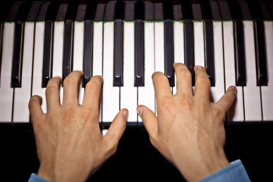 two male hands on the piano. palms lie on the keys and play the keyboard instrument in the music school. student learns to play. hands pianist. black dark background. top view