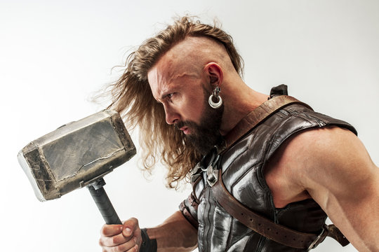 God of thunder. Blonde long hair and muscular male model in leather viking's costume with the big hammer cosplaying Thor isolated on white studio background. Fantasy warrior, antique battle concept.