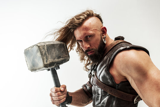 God of thunder. Blonde long hair and muscular male model in leather viking's costume with the big hammer cosplaying Thor isolated on white studio background. Fantasy warrior, antique battle concept.