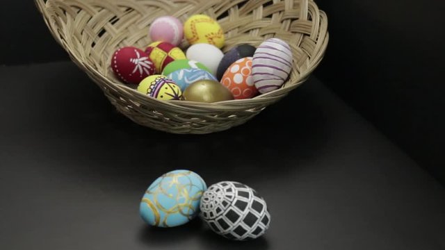 CLOSE-UP: focusing on different Easter eggs in and out of the woven basket over black background
