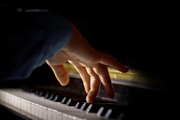 Fototapeta na wymiar one male hand on the piano. The palm lies on the keys and plays the keyboard instrument in the music school. student learns to play. hands pianist. black dark background