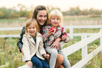 Fototapeta na wymiar Pretty young mother having fun together with her daughters. Happy loving family. Stylish lovely mother with kids. Family enjoing and playing on meadow at autumn sunset background. Fashion family look.