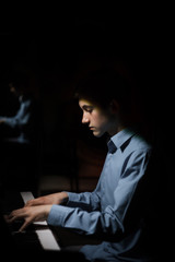 Obraz na płótnie Canvas young man sitting at the piano. boy emotionally plays the keyboard instrument in the music school. student learns to play. hands pianist. black dark background. vertical