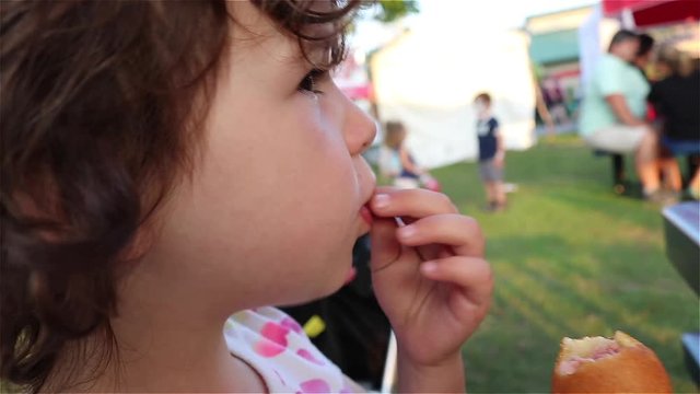 Close up of a young girl eating a corndog at a summer fair