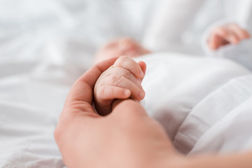 cropped view of mother and baby holding hands