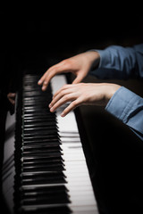 Fototapeta na wymiar two male hands on the piano. palms lie on the keys and play the keyboard instrument in the music school. student learns to play. hands pianist. black dark background. vertical
