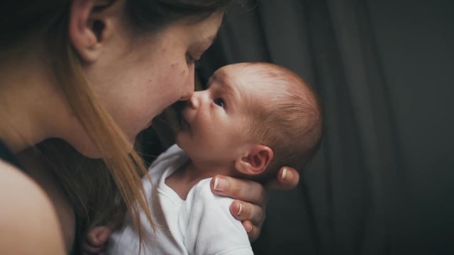 Adorable newborn baby in the arms of his mother. New mom adoring her child as he gazes up at her with wide eyes. Mom rubbing noses with new son in loving moment.