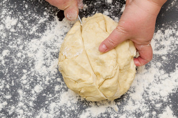 Cutting a large piece of dough on a table with flour for making cottage cheese cookies