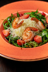 Fresh salad of arugula, shrimp and strawberry. Dark wooden background. Restaurant menu