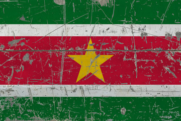 Grunge Suriname flag on old scratched wooden surface. National vintage background.