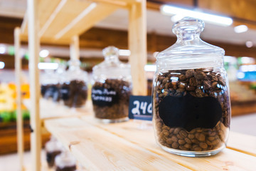 Traditional black coffee beans in a glass jar on the counter of a small market or store. 