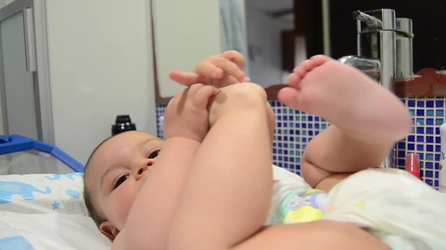 Cute six months old baby boy playing with dummy and his feet in the bathroom.