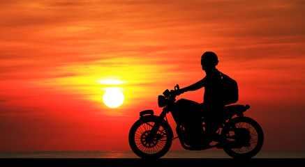 Fototapeta na wymiar Silhouette biker with his motorbike on blurry blue sky background
