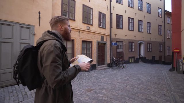 Bearded tourist backpacker discovering old town Stockholm Sweden. Happy handsome tourist exploring Gamla stan with a map. Steadicam footage following the hipster traveler.