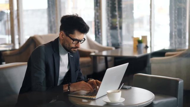 Corporate manager handsome middle-aged man in trendy suit is working in cafe during lunch break using modern laptop typing looking at computer screen.