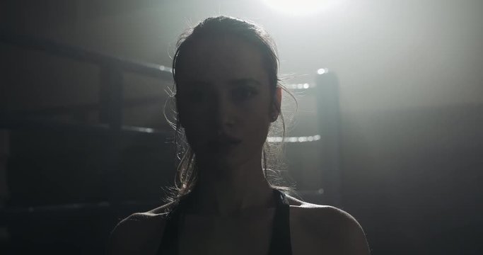 Portrait of tired female boxer standing on the boxing ring and looking at the camera