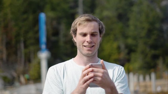 Slow Motion Man Standing Outdoors On Pier In Marina Smiling And Using Smartphone In The Summer